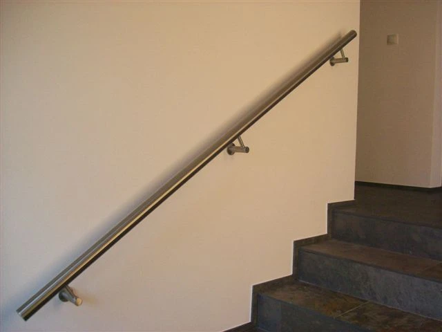 Edelstahl-Wandhandlauf mit drei Trägern an weißer Wand über einer Innentreppe mit dunklen Schieferstufen
